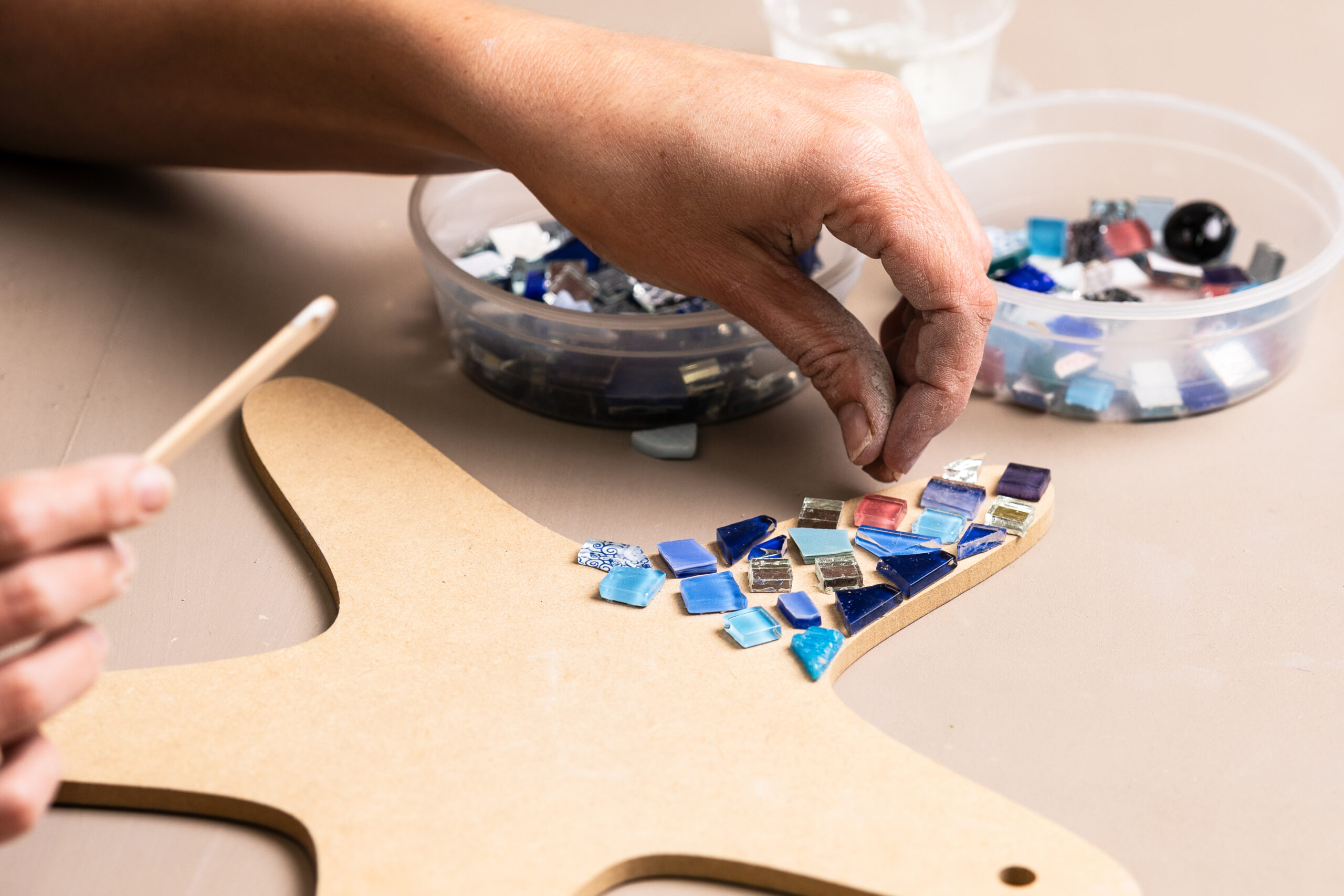 Close-up of a person creating a mosaic artwork with colorful glass tiles on a wooden base at Crafted Clay in Johannesburg.