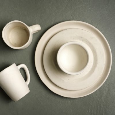 Handmade unglazed ceramic tableware, including a plate, bowl, and mugs, crafted at Crafted Clay in Johannesburg.
